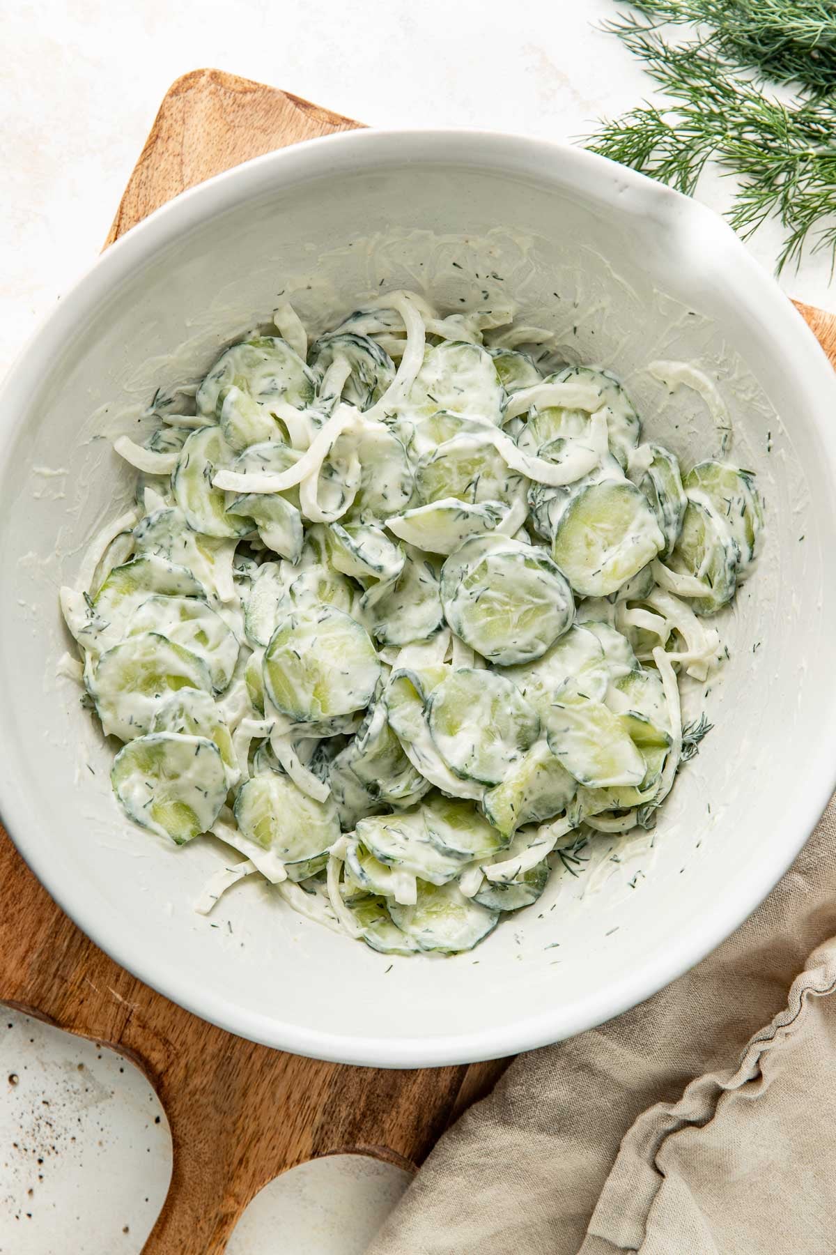 Overhead view of a white bowl of Creamy Cucumber Salad topped with fresh dill.