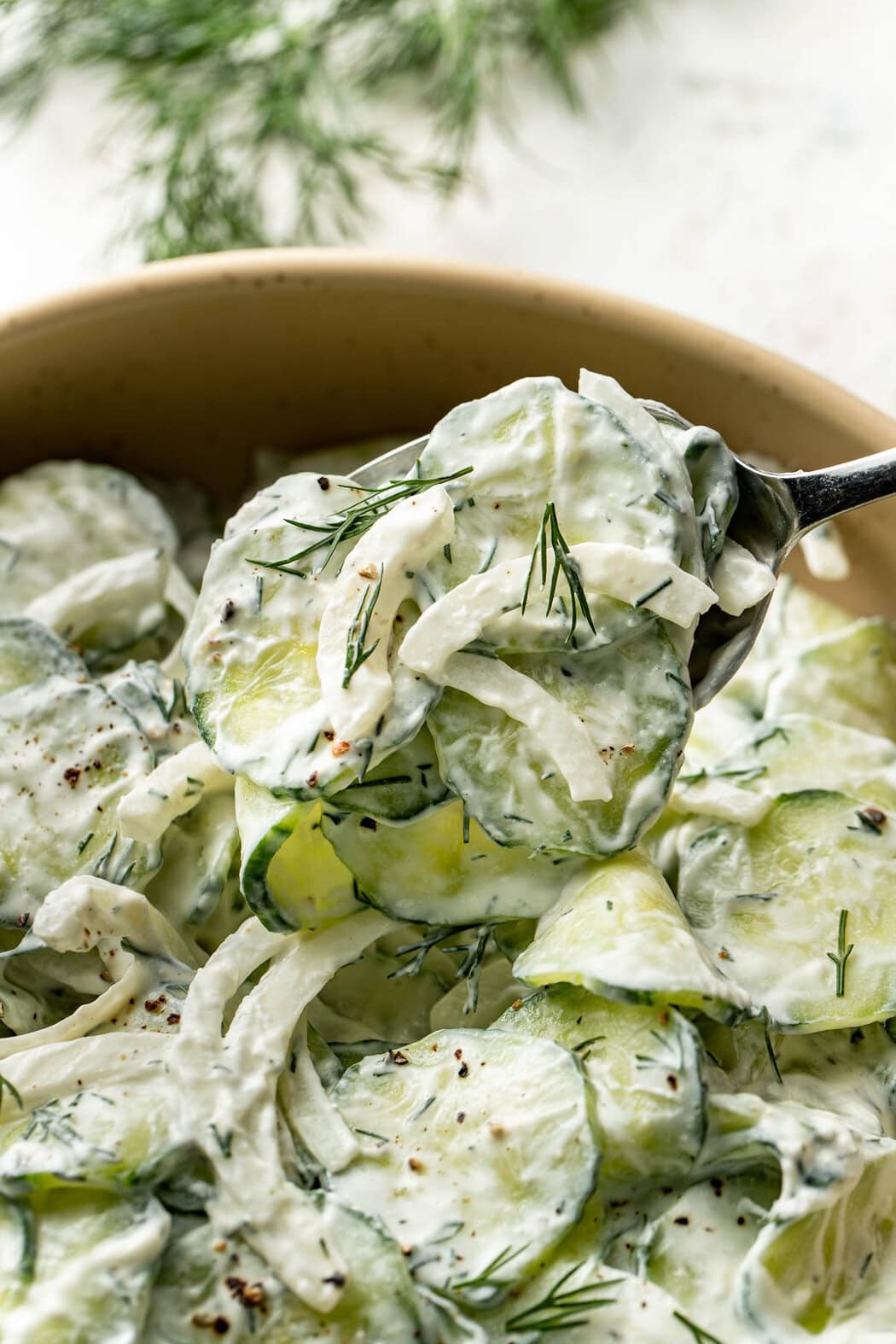Close up view of a spoonful of Creamy Cucumber Salad over a bowl.