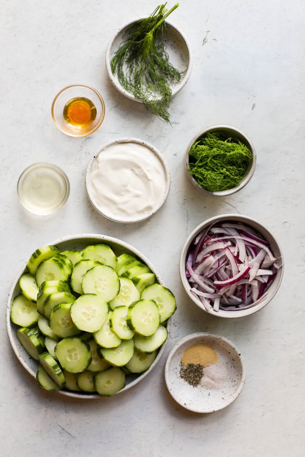 Overhead view of small bowls filled with ingredients for making a creamy cucumber salad. 