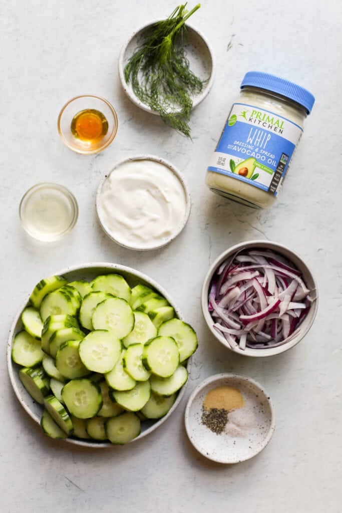 Overhead view all ingredients for creamy cucumber salad on white background