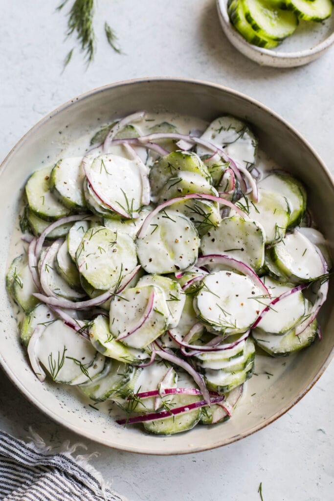 Close up view creamy cucumber salad with red onion served in stone bowl