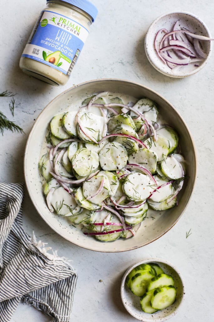 Creamy cucumber salad in shallow stone bowl with red onion and fresh dill sprinkled on top