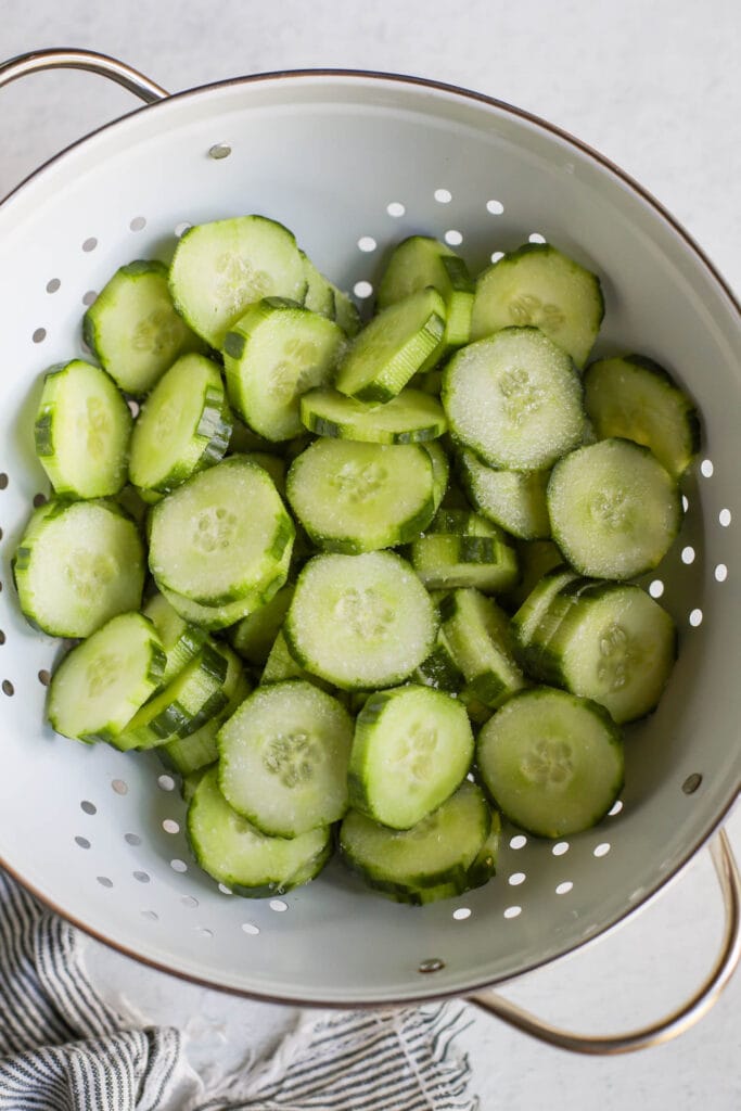 Sliced cucumbers with salt sprinkled on top in white colander 