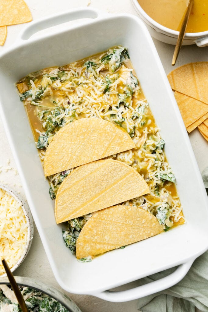 Process image of green chicken enchilada casserole with layering corn tortillas on mixture in white baking dish