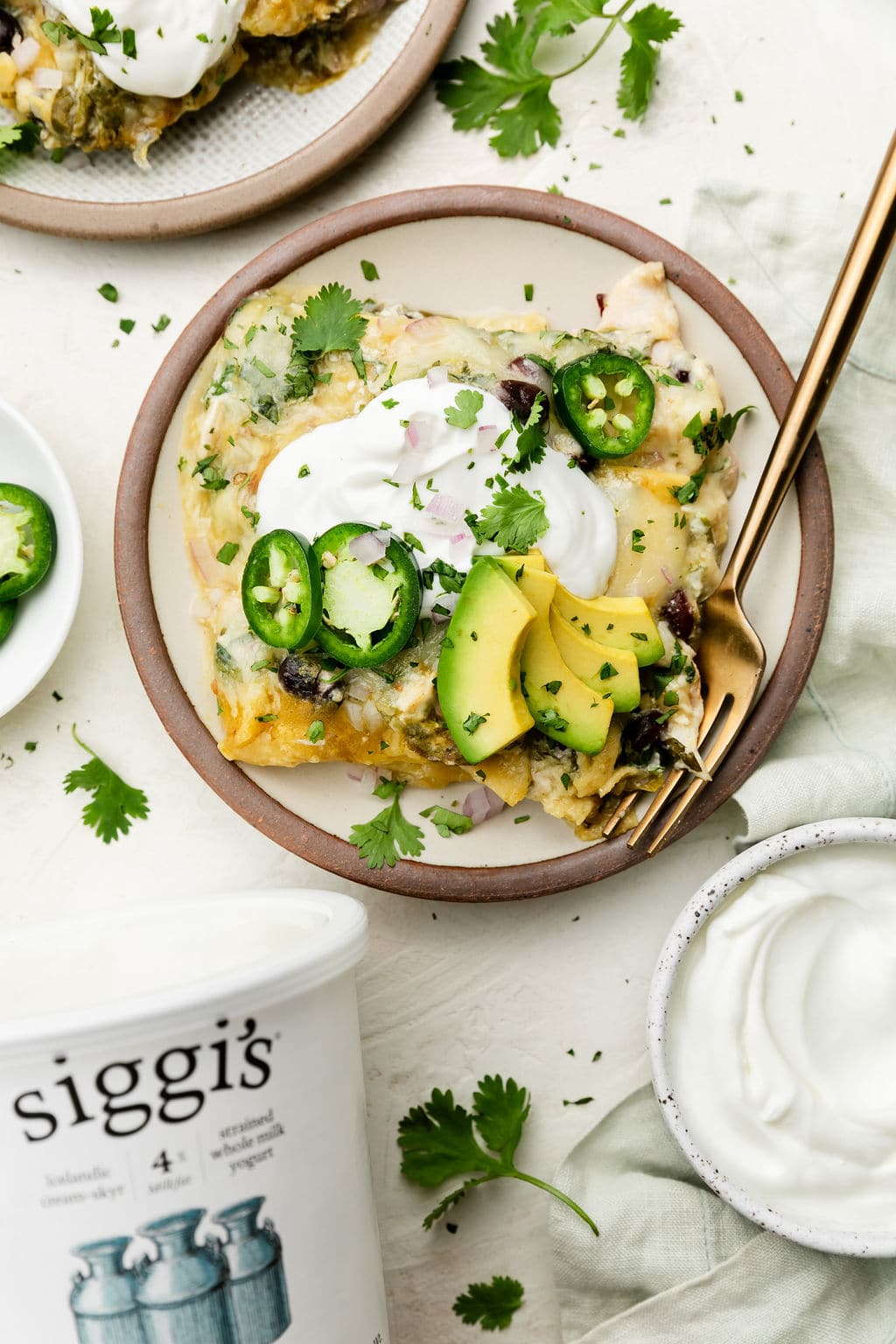 Serving of green chicken enchilada casserole on plate topped with yogurt and avocado slices
