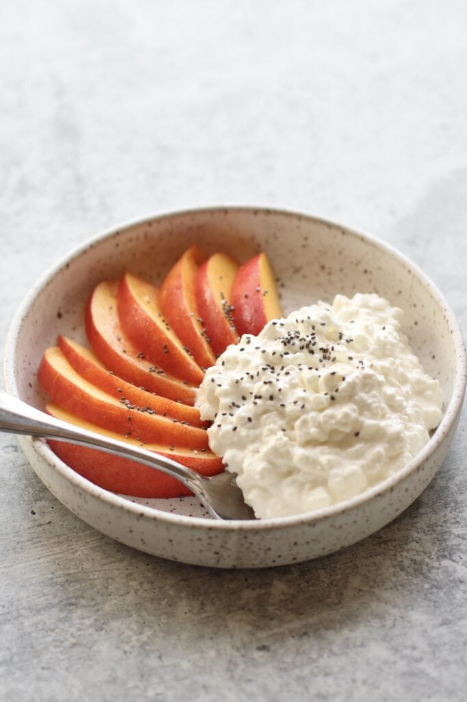 Close up view of a white bowl filled with sliced fruit and cottage cheese topped with chia seeds. 