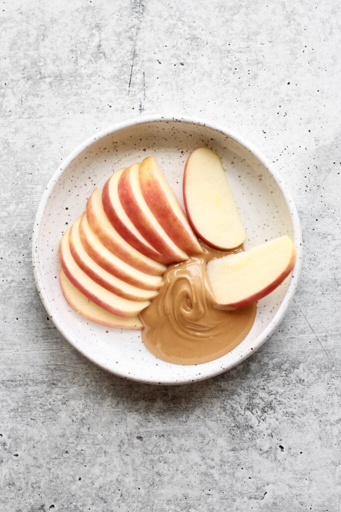 Apple slices with peanut butter on shallow stone bowl