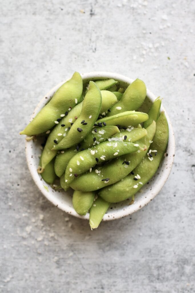 Small stone bowl overfilled with edamame sprinkled with seasoning for healthy snacks