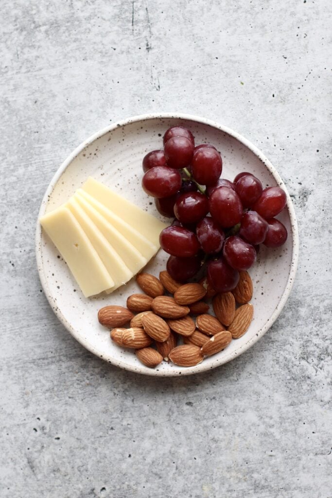 stone plate with servings of raw almonds, red grapes, and slices of cheese for healthy snacks