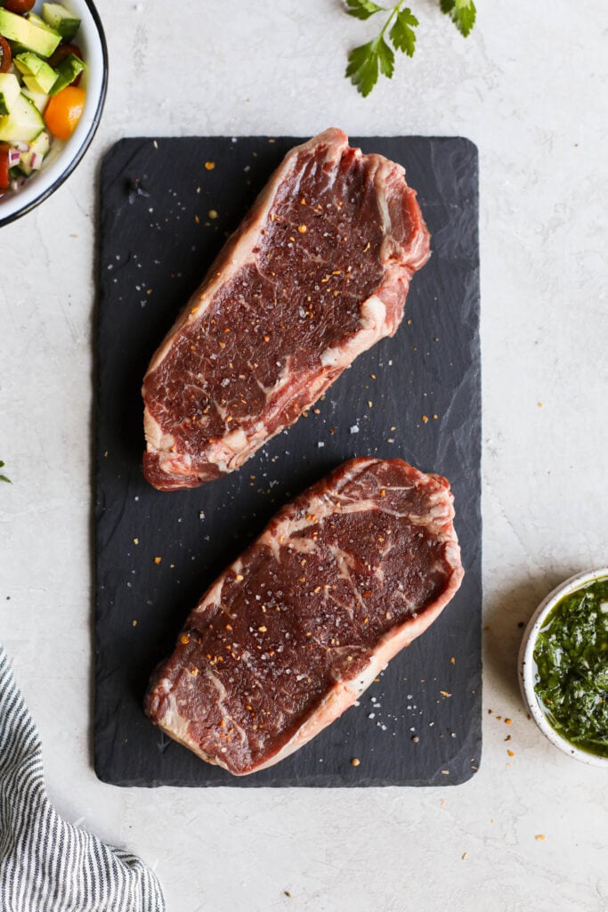 Raw grass fed beef steaks on black cutting board
