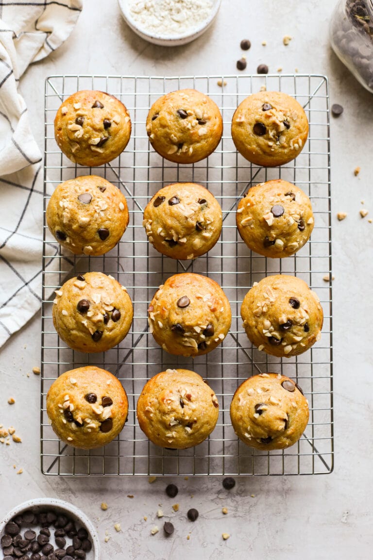 Overhead view of a cooling rack filled with freshly baked peanut butter protein muffins topped with chocolate chips and peanut pieces. 