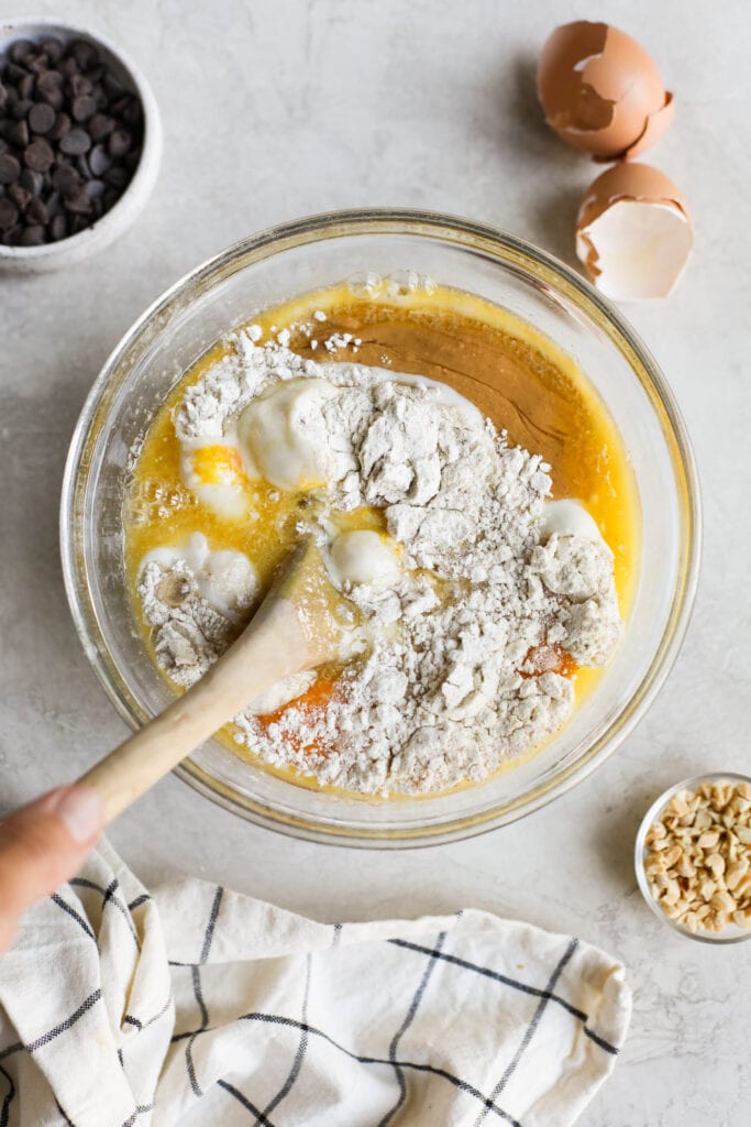 Overhead view of a mixing bowl filled with baking ingredients being stirred with a wooden spoon. 