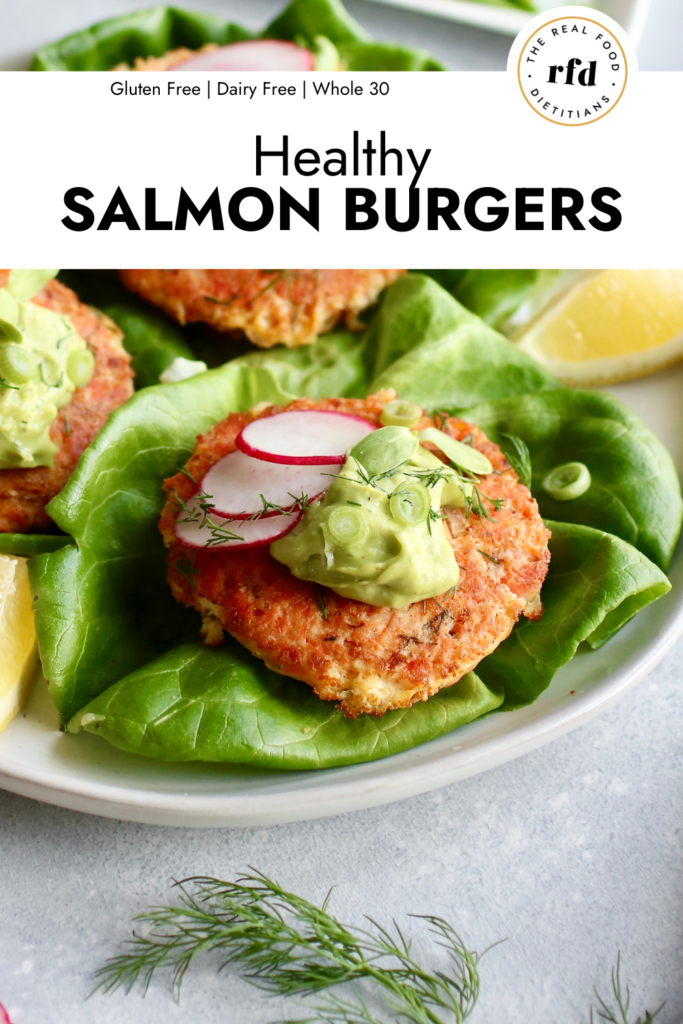 Close up side view salmon burger on lettuce topped with avocado garlic sauce and sliced radishes