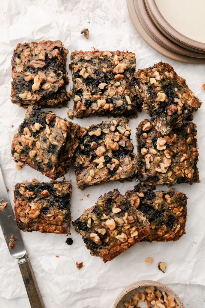 Batch of oatmeal breakfast bars with wild blueberries and walnuts cut into squares on parchment paper