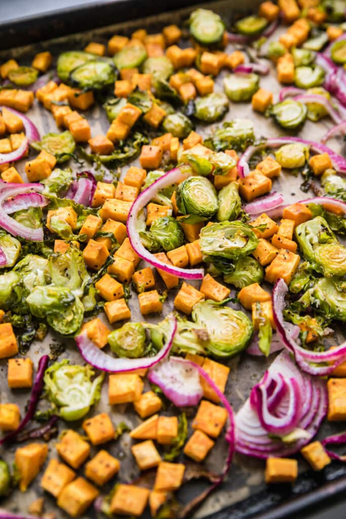 Roasted Brussels sprouts, butternut squash and red onion slices on a baking sheet