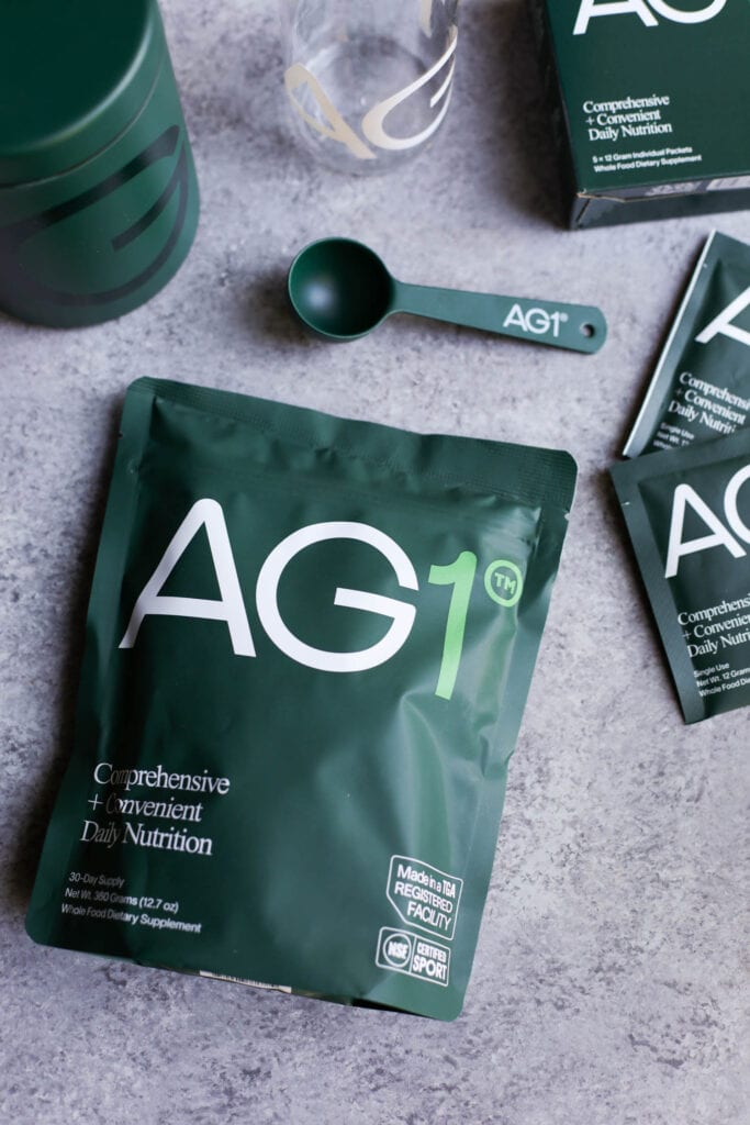 A pouch of AG1 supplements and a branded AG1 scoop.