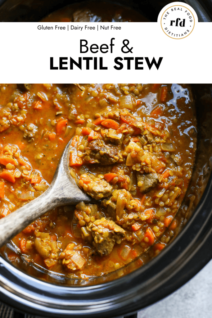 Wooden spoon scooping up serving of beef and lentil stew from black slow cooker