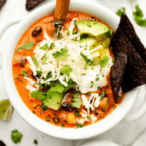 Overhead view white bowl filled with taco soup topped with sour cream, diced avocado, and cilantro