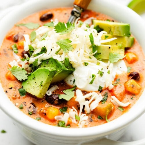 Close up view of a bowl of taco soup topped with avocado pieces and melted cheese.