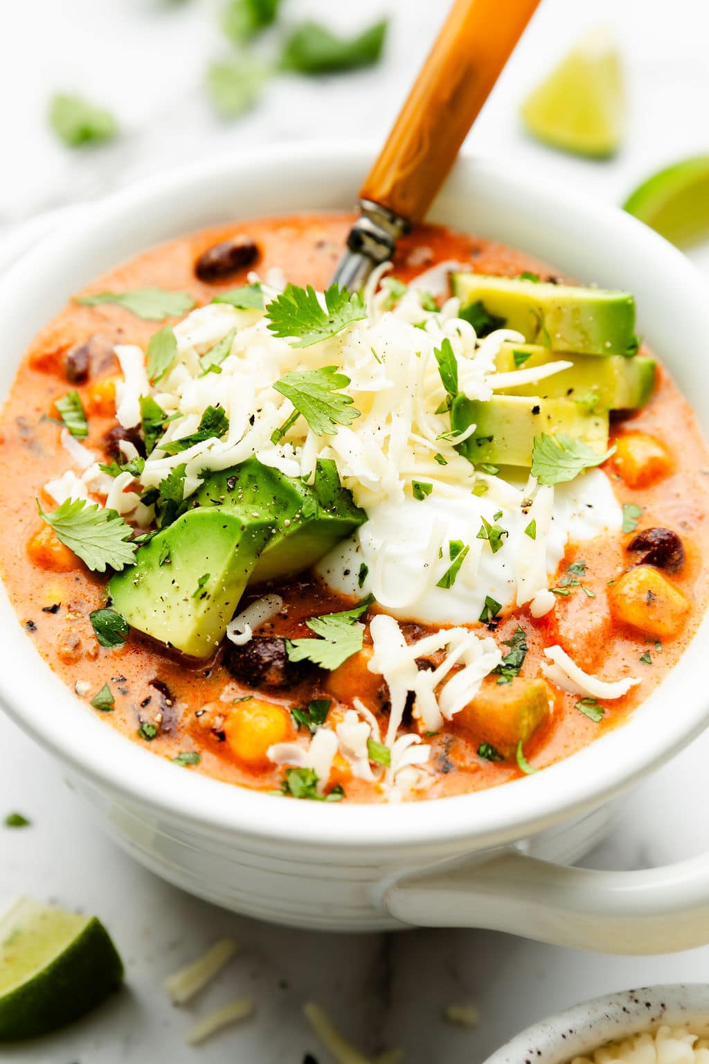 Close up view taco soup in white bowl topped with sour cream, avocado, cheese and cilantro