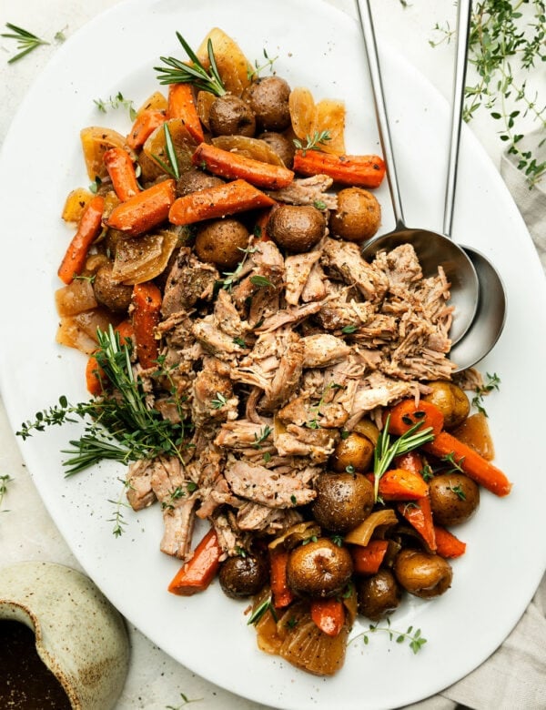 White platter filled with crockpot pork roast shredded with roasted potatoes and carrots on either ends of platter