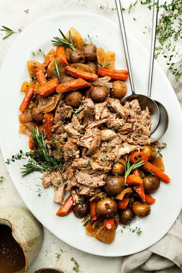 White platter filled with crockpot pork roast shredded with roasted potatoes and carrots on either ends of platter