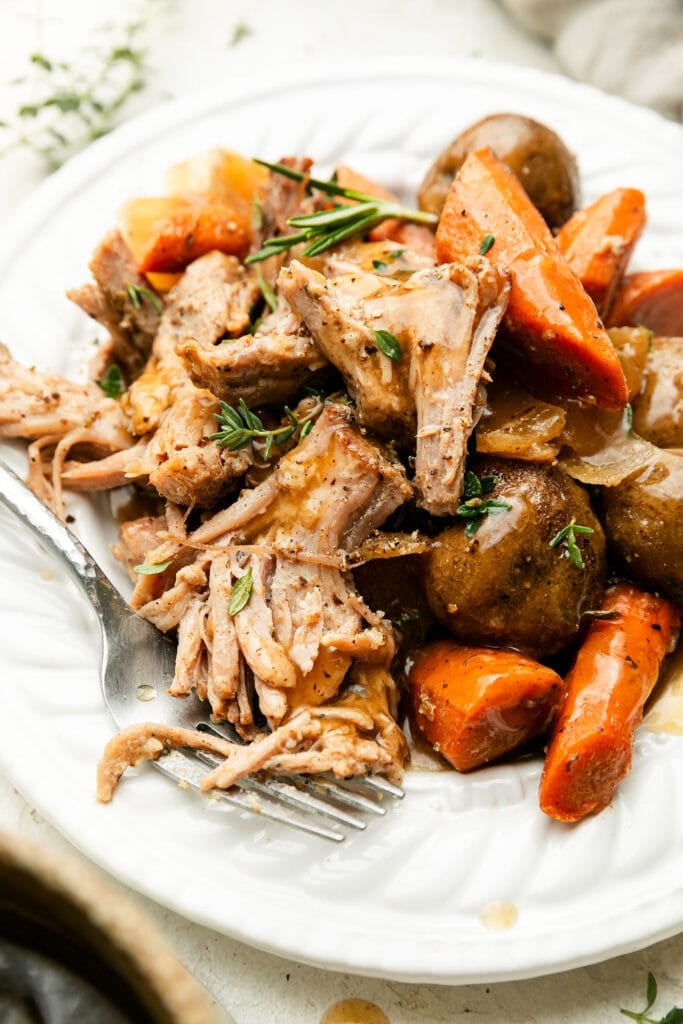A plate of crock pot pork roast with carrots and potatoes.
