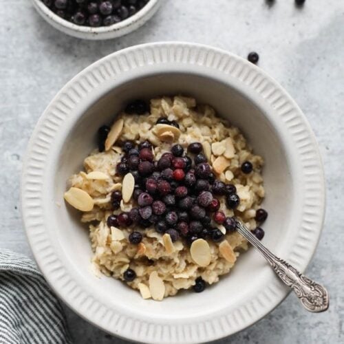 Overhead view white bowl filled with oatmeal topped with high fiber wild blueberries and sliced almonds