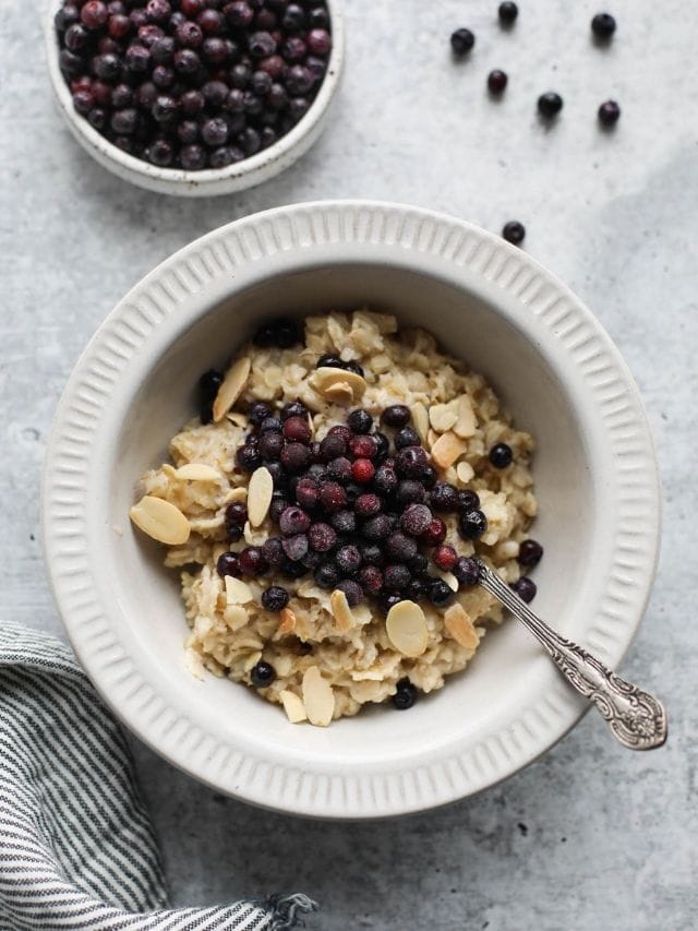 A white bowl filled with oatmeal topped with high fiber wild blueberries and sliced almonds.