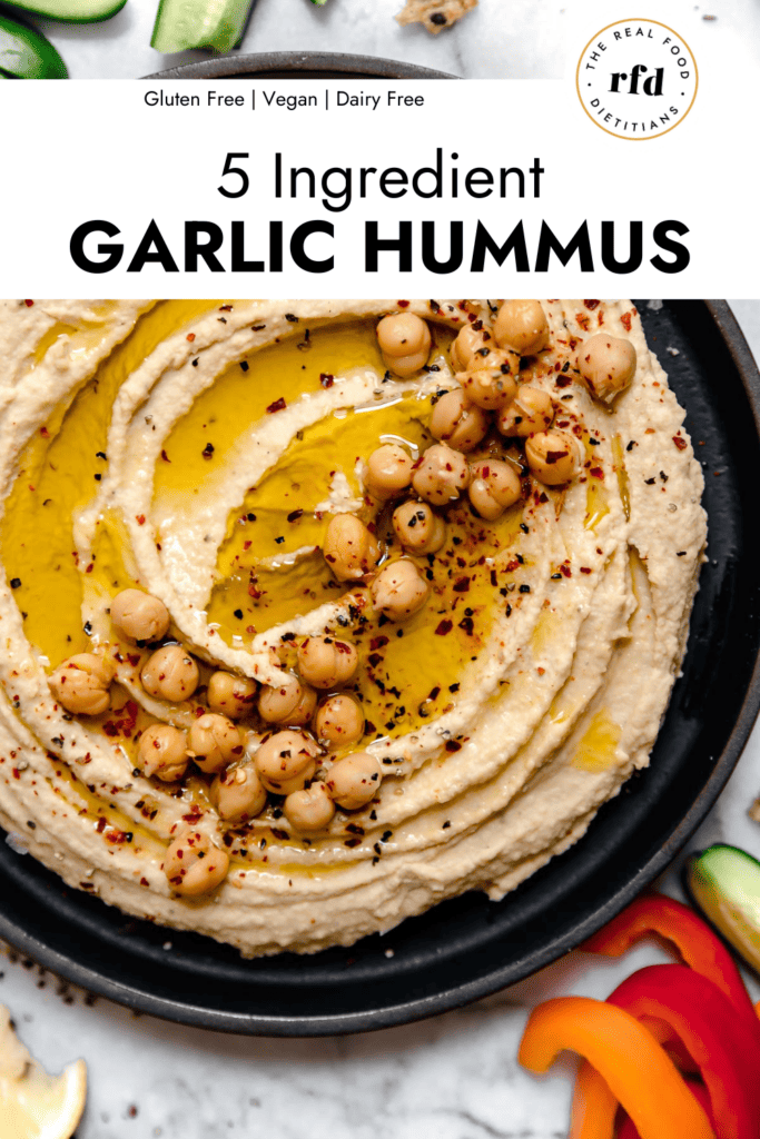 Overhead view homemade garlic hummus in black bowl topped with chickpeas, olive oil, and cracked black pepper