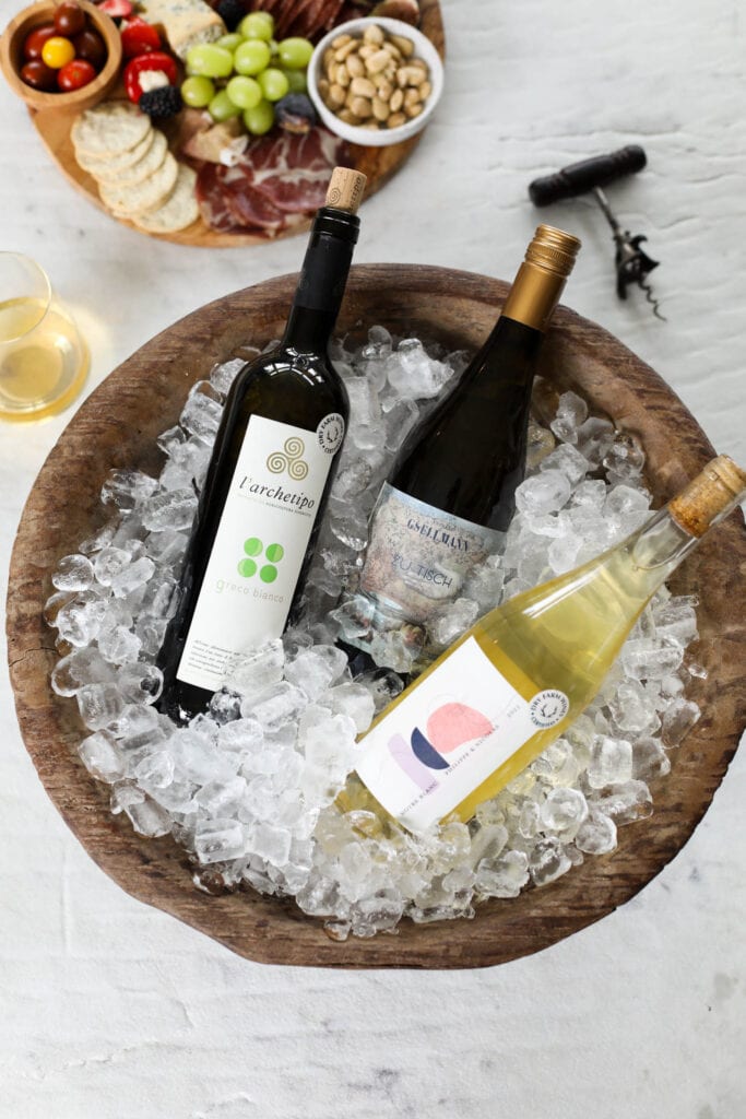 Three bottles of wine with Dry Farm Wines round logo on each, bottles of win on ice in wooden bowl