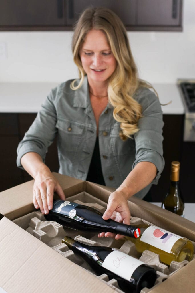 A women wearing black dress and jean jacket removing bottle of wine from packaging