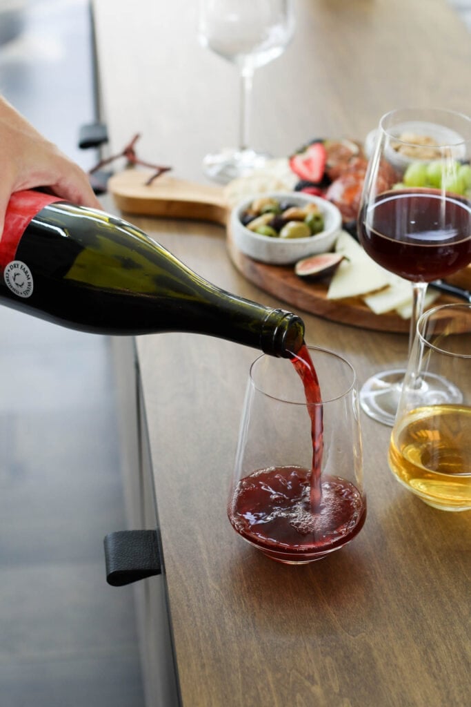 Red wine being poured into wine glass on wooden countertop with charcuterie board in background