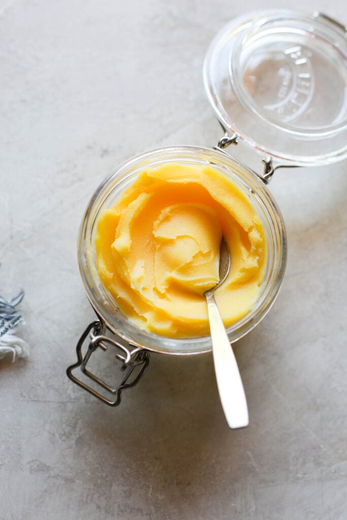 A jar of homemade ghee with spoon scooping up spoonful