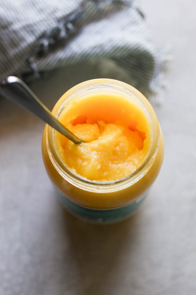 A jar of store bought ghee with a spoon in it. 