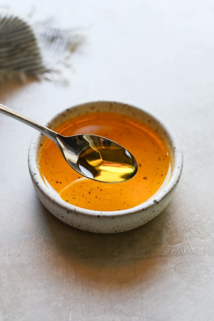 A small dish of golden yellow melted ghee with a spoonful hovering above. 