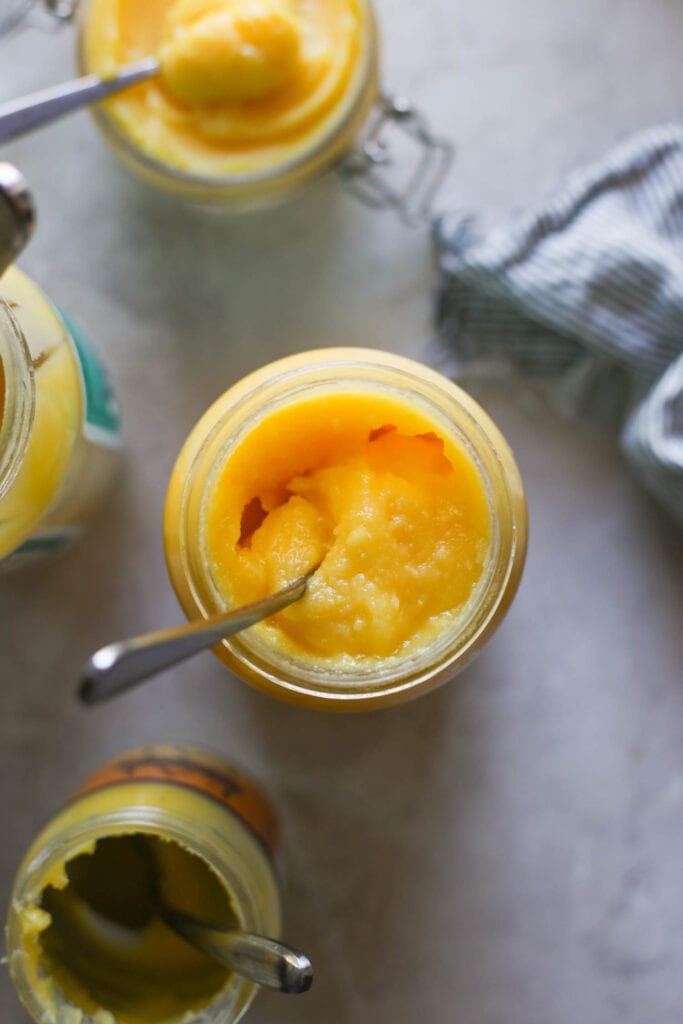Multiple jars of ghee, both store bought and one homemade, with spoons in them. 