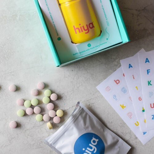 Overhead view Hiya kids vitamins in packaging with refill packet in front, open with chewable tables spilling out