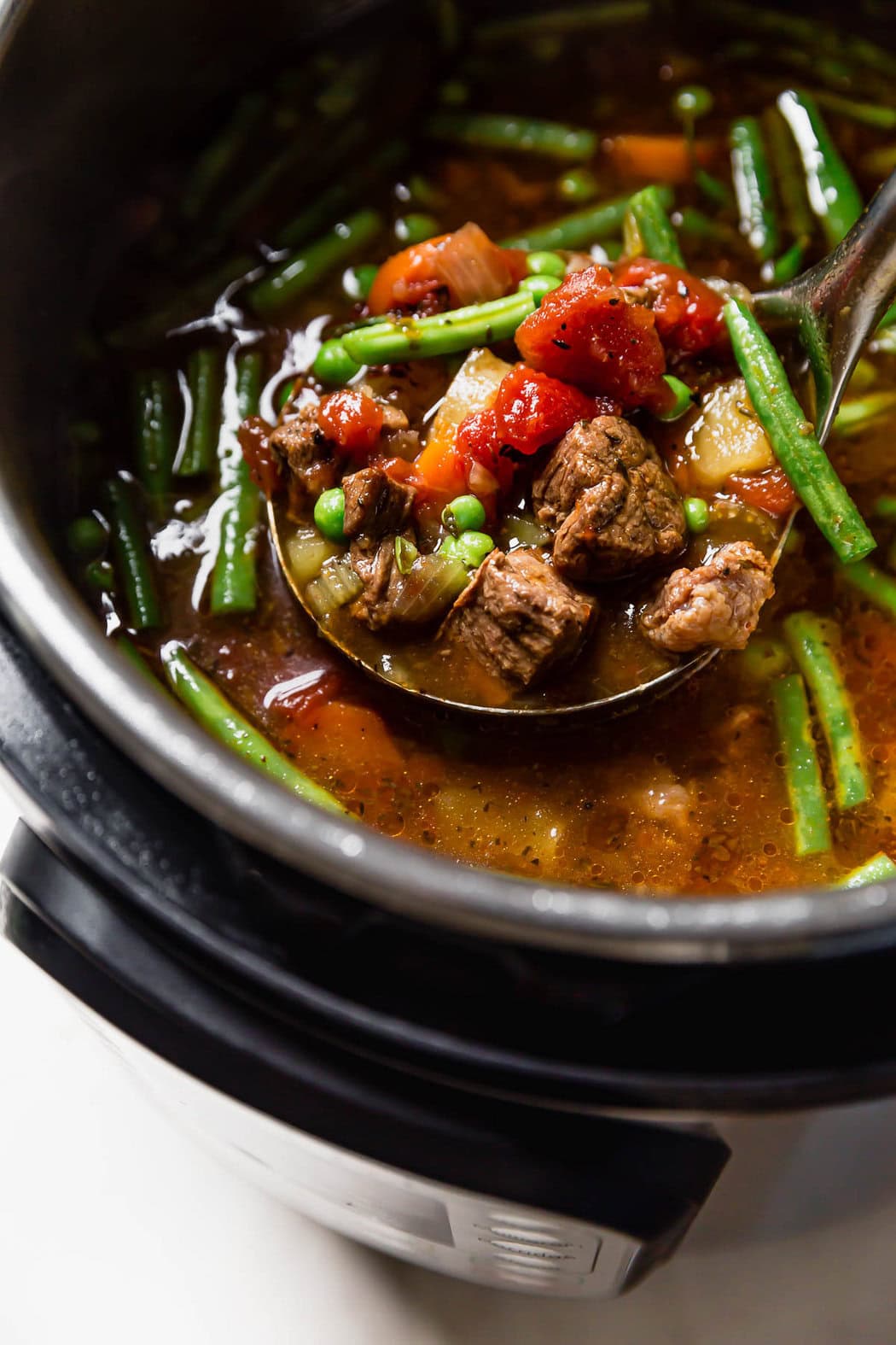 Ladle filled with scoop of vegetable beef soup over an instant pot