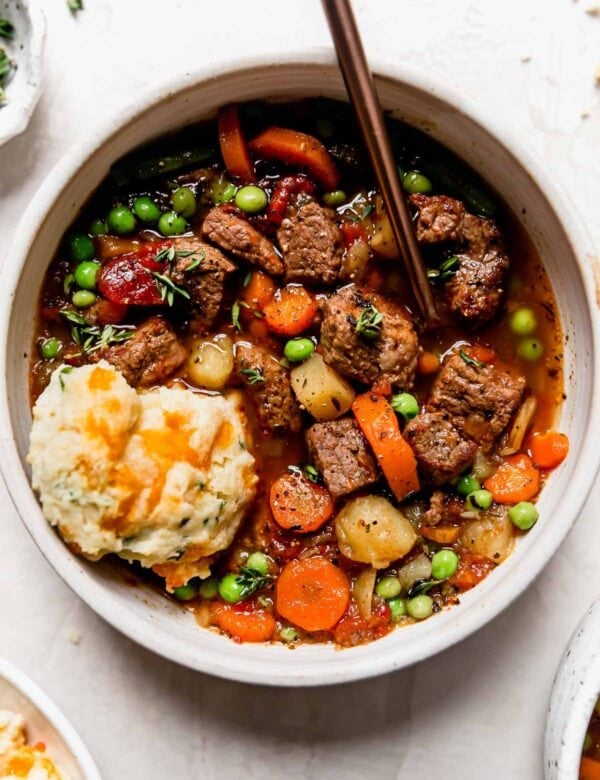 Overhead view white bowl filled with vegetable beef soup with cheesy biscuit on top