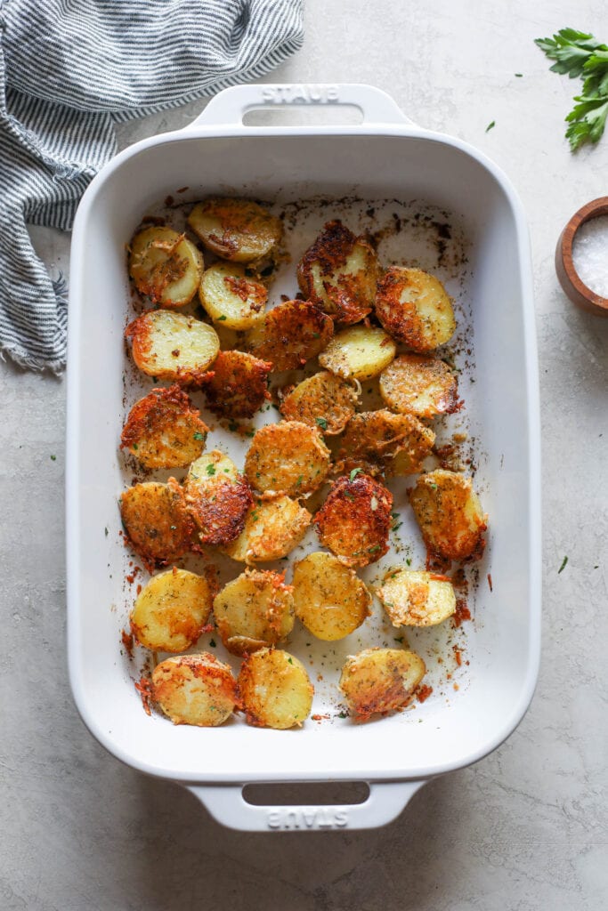 White baking dish filled with side dish of Parmesan Crusted Potatoes topped with a few fresh herbs