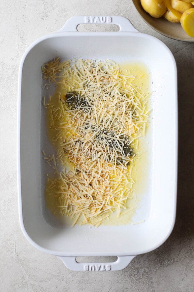 Overhead view white baking dish with melted butter, seasonings and shredded Parmesan cheese in bottom of dish
