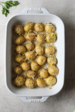 Overhead view potato halves coated in butter, seasonings and Parmesan cheese places cut-side down in white baking dish