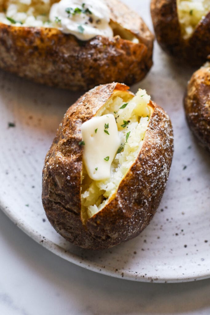A close up of a perfectly baked potato, revealing the kosher salt on the crispy skin and butter melting inside. 
