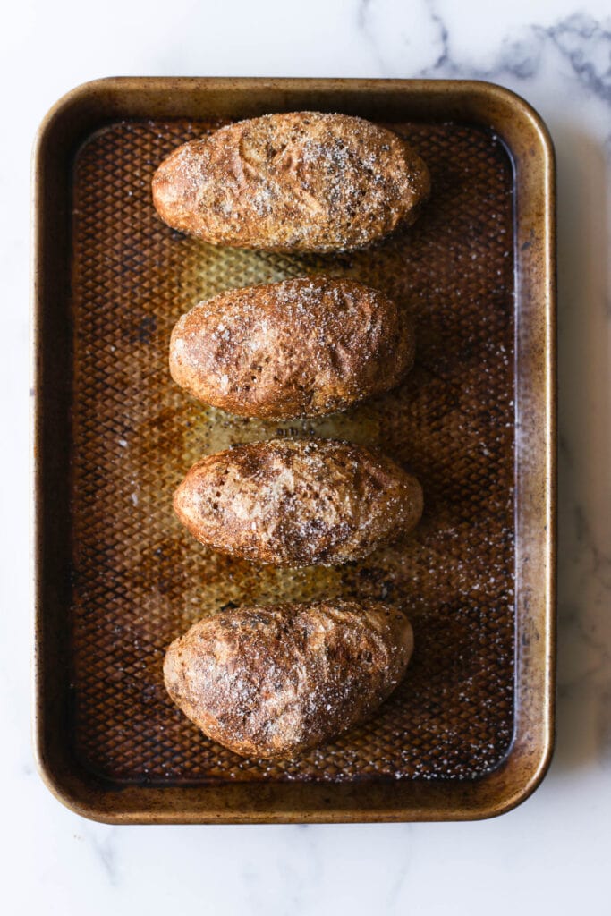 Four perfectly baked potatoes in vertically aligned in a baking dish. 