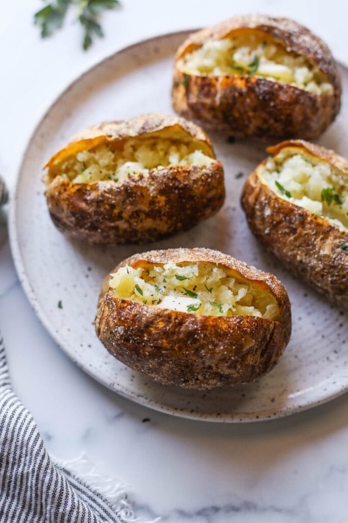 A photo of four baked potatoes with perfectly crispy salted skin on a plate.