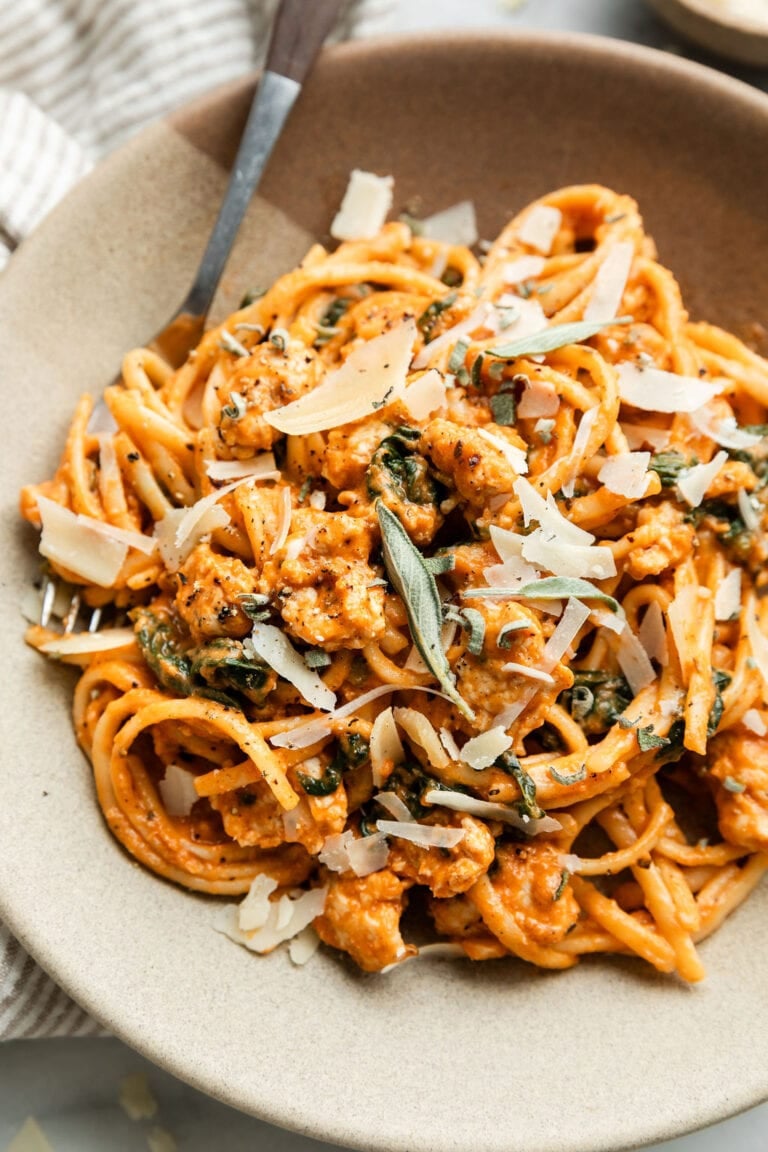 Overhead view pumpkin pasta with sausage in bowl topped with shaved parmesan