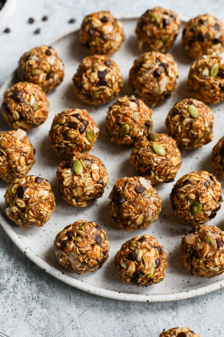 Overhead view of pumpkin spice protein balls filled with pumpkin seeds and chocolate pieces on a white plate. 