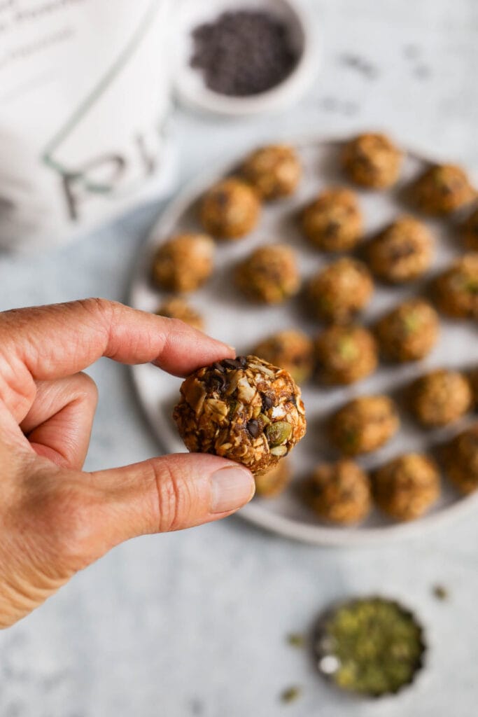 A single pumpkin protein ball being held up over a platter filled with pumpkin protein bites
