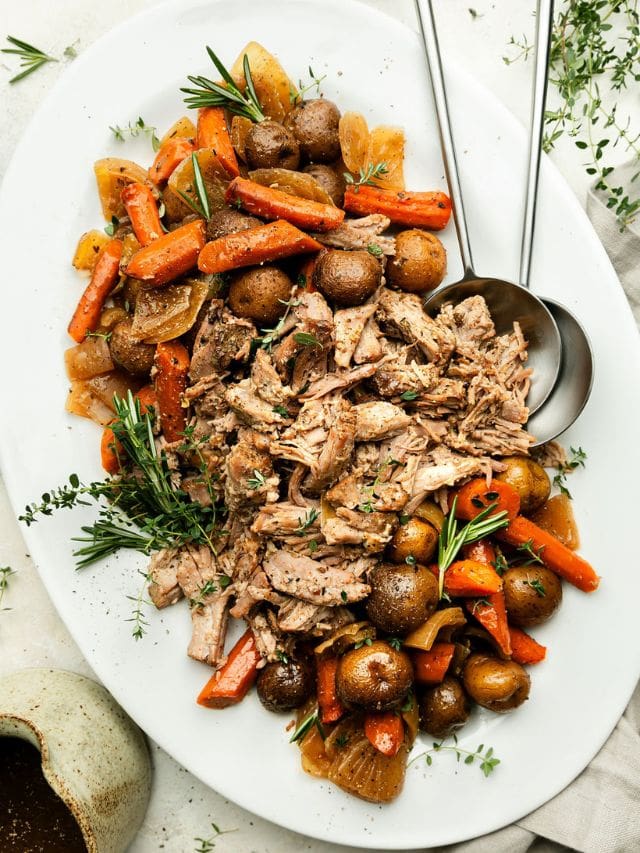 Overhead view white platter filled with slow cooker pork roast, baby potatoes, and roasted carrots.